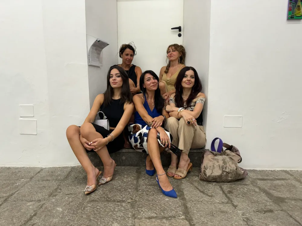 Cinque donne sedute su un gradino davanti a una porta bianca nella galleria