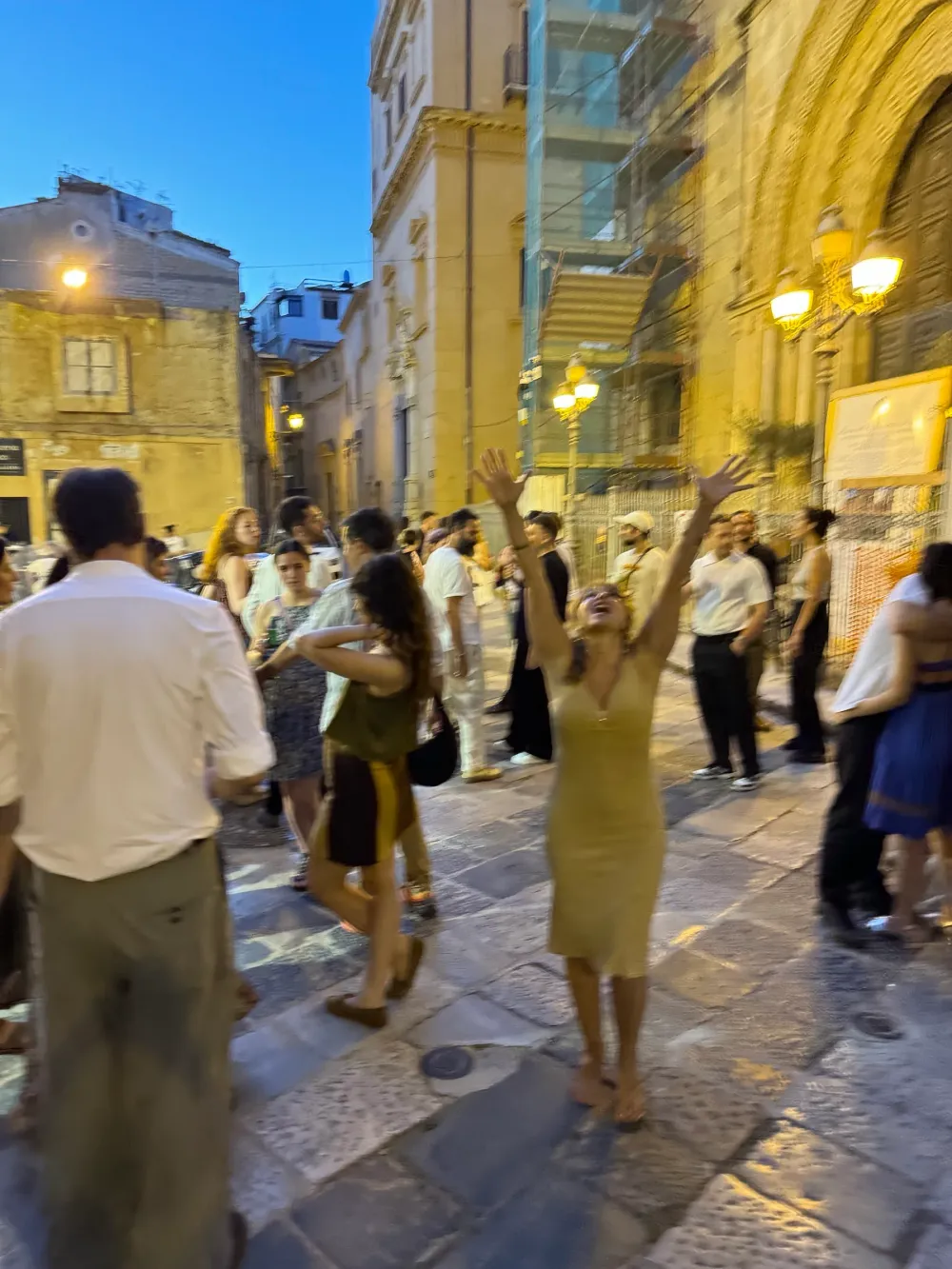 Una donna alza le braccia in festa tra la folla in piazza, a sera