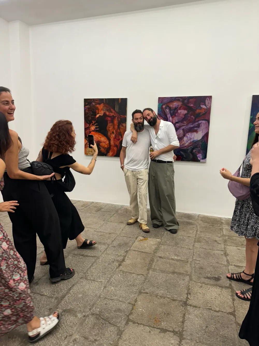 Un gruppo di persone sorridenti in sala, davanti a tre dipinti