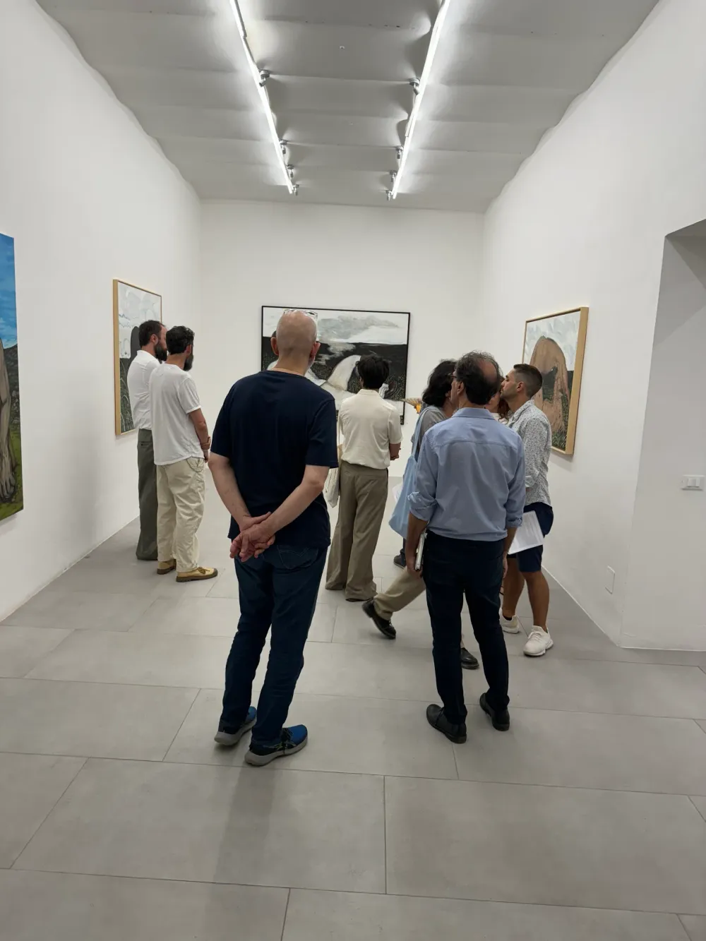 Visitatori osservano i dipinti in una sala bianca