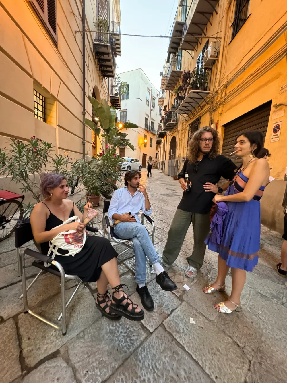 Persone sedute e in piedi in via Maletto nella luce del tramonto