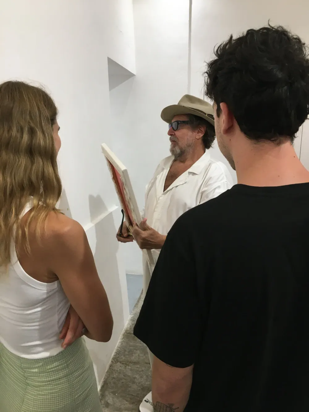 Julian Schnabel con un piccolo dipinto in mano parla con due giovani visitatori