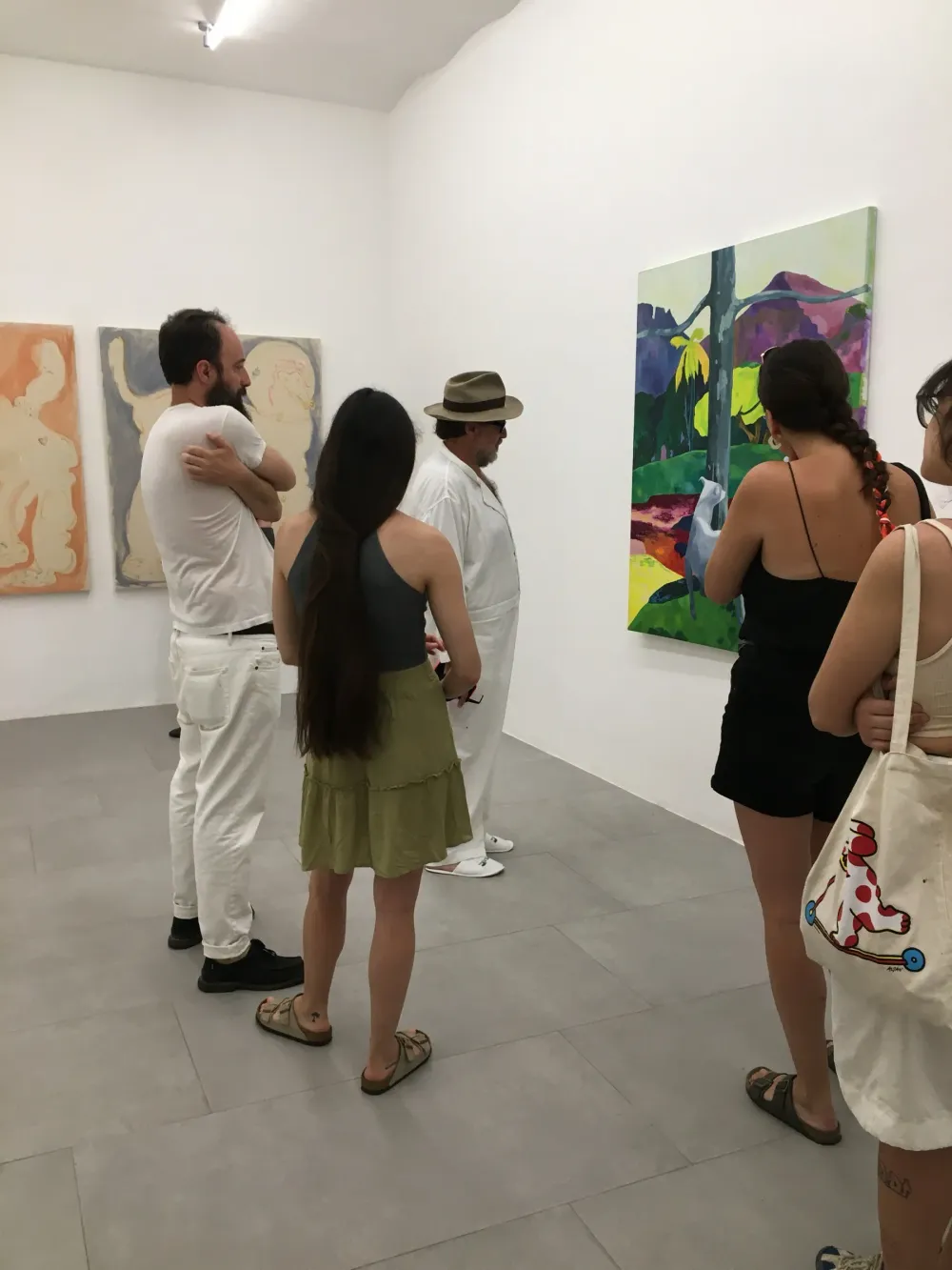 Julian Schnabel e alcuni visitatori in una sala con dipinti a toni pastello e un paesaggio con due cani