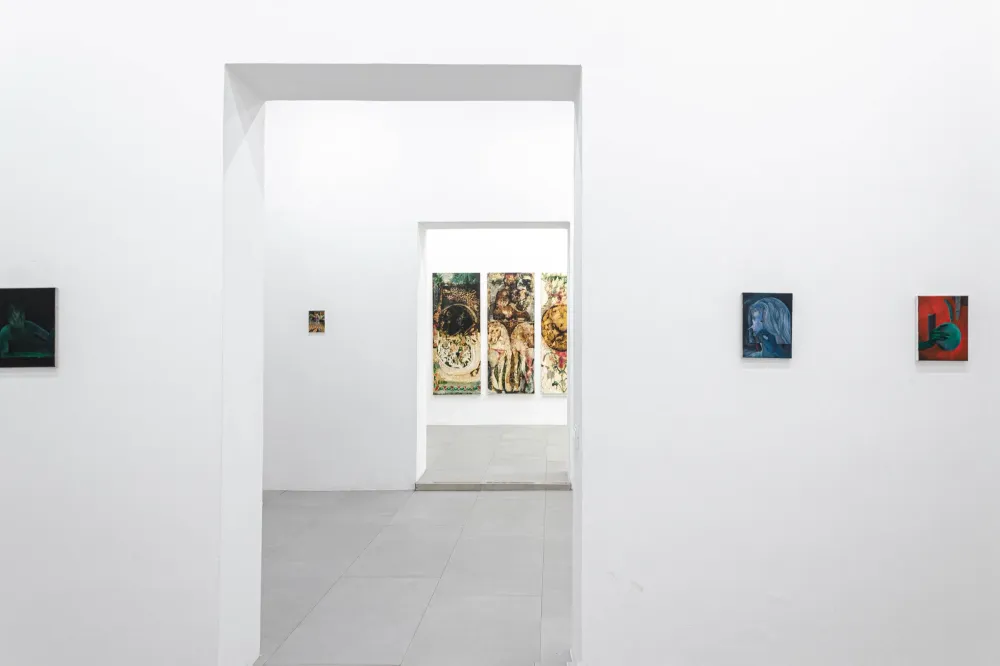 Sala bianca con piccoli dipinti alle pareti; attraverso due porte in fila si vede in fondo un trittico